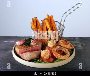 Steak und Pommes Frites mit panierten Pilzen und Zwiebelringen. Stockfoto