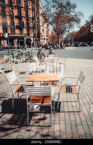 Eine vertikale Aufnahme eines sonnendurchfluteten Cafés in einer belebten Stadt Barcelona mit leeren Tischen und Stühlen, die zu einem Moment der städtischen Entspannung einladen Stockfoto
