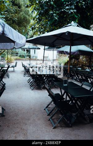 Abgeschiedenes Café im Freien unter Sonnenschirmen in einem schattigen Park gelegen, bietet eine ruhige Umgebung zum Essen. Leere Tische erwarten Besucher, vielversprechend Stockfoto