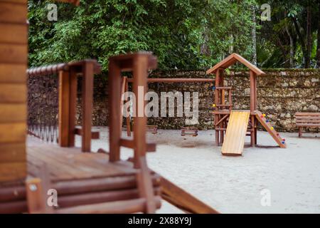 Abgeschiedener Kinderspielplatz in einem üppigen tropischen Park mit Holzkonstruktionen wie Rutschen und Schaukeln. Die friedliche Umgebung bietet Stockfoto