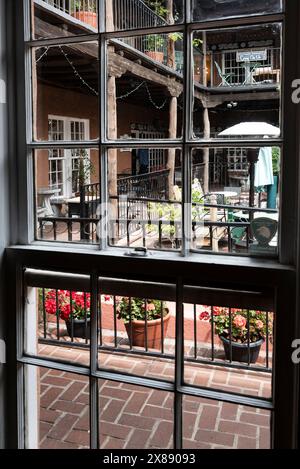 Blick durch das Fenster auf mehrstöckige Wohnhäuser und Kaffeehaus mit Sitzgelegenheiten im Freien und Blumentöpfen in Las Cruces, NM Stockfoto