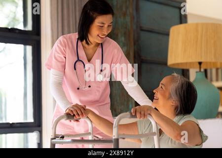 Asiatische junge Krankenschwester bei rosafarbener Patientin mittleren Alters zu Hause Stockfoto