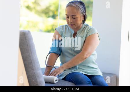 Eine asiatische Frau mittleren Alters, die zu Hause den Blutdruck kontrolliert Stockfoto