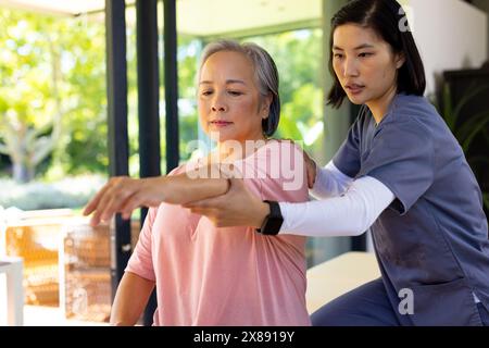 Zu Hause dehnen asiatische junge Krankenschwester und Patienten mittleren Alters gemeinsam Arme Stockfoto