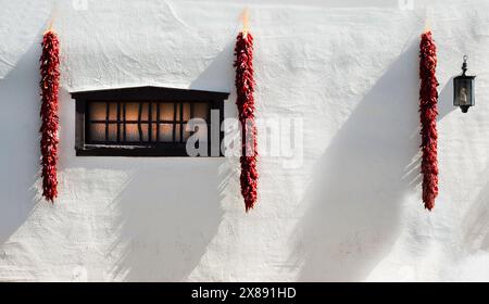 Seitliche Beleuchtung der roten Chiliristras, die an der weißen Wand an der Außenseite des traditionellen Wohnsitzes im Süden New Mexikos in Mesilla, NM, USA hängen Stockfoto