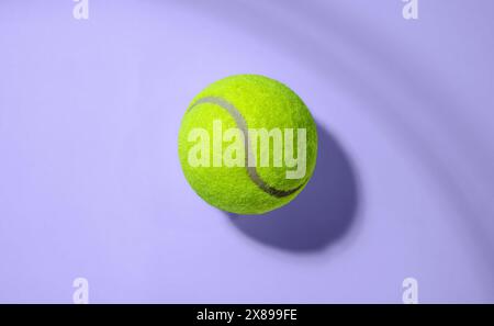 Leuchtend gelber Tennisball ist vor einem massiven violetten Hintergrund sichtbar und zeigt ein kontraststarkes Bild mit minimalistischem Ansatz, ideal Stockfoto