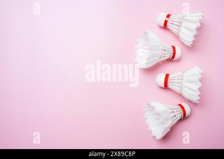 Flache Anordnung von drei weißen Badminton-Shuttlecocks mit roten Details, die diagonal auf einem leuchtend rosa Hintergrund angeordnet sind, bieten Platz für Text oder Design e Stockfoto