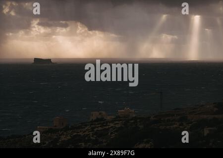 Dunkle Wolken sammeln sich über dem Meer, mit Sonnenstrahlen, die durchbrechen und die ferne Küste beleuchten Stockfoto