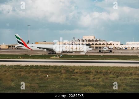 Ein Emirates-Flugzeug, das auf dem Vorfeld am Malta International Airport, Malta, mit Sichtbarkeit des Terminalgebäudes dahinter fährt Stockfoto