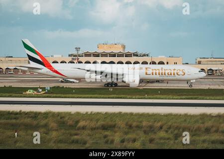 Ein Emirates-Flugzeug, das auf dem Vorfeld am Malta International Airport, Malta, mit Sichtbarkeit des Terminalgebäudes dahinter fährt Stockfoto