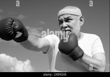Schöner älterer Mann, der Boxtritte übt. Ein älterer Mann schlägt einen Boxsack. Ältere Männer kämpfen gegen Posen. Senior Sportmann mit Boxhandschuhen. Stockfoto