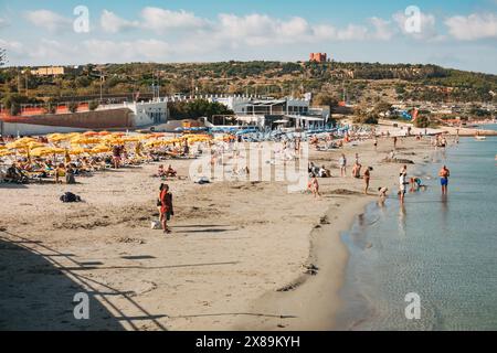 Schwimmer und Sonnenanbeter nutzen Liegestühle und Sonnenschirme am Mellieha Bay Beach, Malta Stockfoto