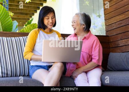 Asiatische Mutter und Tochter mittleren Alters lachen zu Hause über Laptop Stockfoto