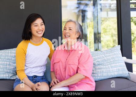 Zu Hause sitzen asiatische Mutter und Tochter mittleren Alters und lächeln zusammen Stockfoto