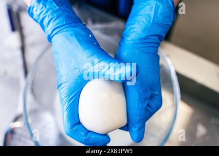 Nahaufnahme von Mozzarella-Käse-Rollen mit blauhandgefertigten Händen. Der Prozess der Herstellung von italienischem Käse. Hochwertige Fotos Stockfoto