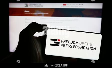 Person, die ein Mobiltelefon mit dem Logo der Organisation „Freedom of the Press Foundation“ (FPF) vor der Webseite hält. Schwerpunkt auf dem Display des Telefons. Stockfoto