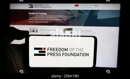 Person, die ein Mobiltelefon mit dem Logo der Organisation Freedom of the Press Foundation (FPF) vor der Webseite hält. Schwerpunkt auf dem Display des Telefons. Stockfoto