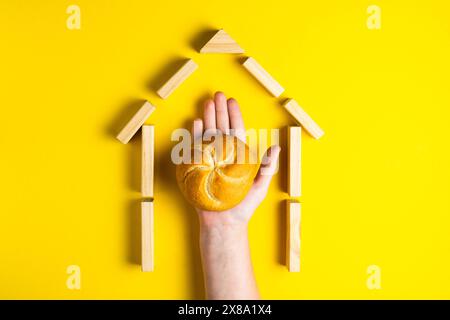 Hand hält Geldmünzen in der Nähe von Brot auf gelbem Hintergrund Stockfoto