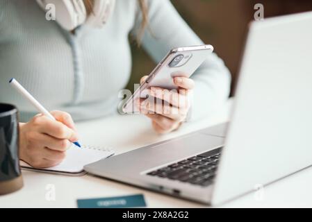Kiew, Ukraine. Januar 2022. Nahaufnahme einer Frau mit Handy und Laptop auf weißem Schreibtisch im modernen Büro. Stockfoto