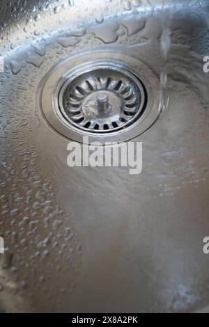 Waschbecken aus Edelstahl und Wasserablauf in einer modernen Küche, Wasserfluss in der Küchenspüle, Wasser fließt aus dem Abfluss Stockfoto