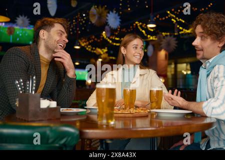 Junge Freunde essen Pizza und trinken Bier, während sie sich im Pub ausruhen Stockfoto