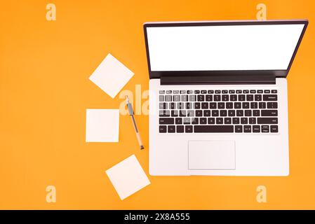 Draufsicht eines Arbeitsplatzes mit Haftnotizen und Stift, leerer Arbeitsbereich auf gelbem Tischhintergrund. Platzieren Sie Text auf einem Laptop-Bildschirm. Stockfoto