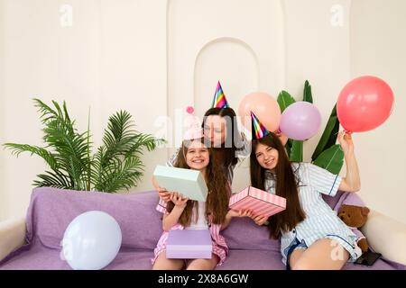Eine glückliche Familie feiert einen Geburtstag mit Geschenken und Ballons auf einer lila Couch. Stockfoto