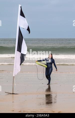 Eine reife Surferin, die ihr Surfbrett trägt und am Towan Beach in Newquay in Cornwall in Großbritannien aus dem Meer wandert. Stockfoto
