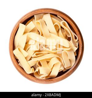 Sagnette, glatte Bandnudeln, in einer Holzschale. Ungekochte, kurze dicke Nudelbänke, laminierte Teigwaren aus Hartweizengrieß und Ei. Stockfoto