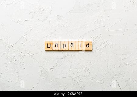 UNBEZAHLTES Wort auf Holzblock geschrieben. UNBEZAHLTER Text auf Zementtisch für Ihr Design, Konzept. Stockfoto