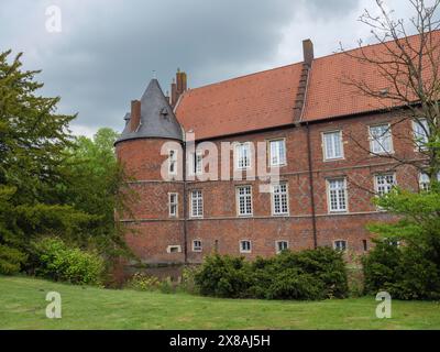 Großes Backsteingebäude mit Dach und Turm, umgeben von grüner Hecke und bewölktem Himmel, rotes Backsteinschloss mit runden Türmen und einem Graben und vielen Bäumen, Stockfoto