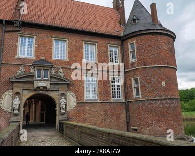 Historische Burg mit Backsteinmauern, einem Bogengang und Statuen, umgeben von Natur, rote Backsteinburg mit runden Türmen und mit einem Graben und vielen Bäumen, sie Stockfoto