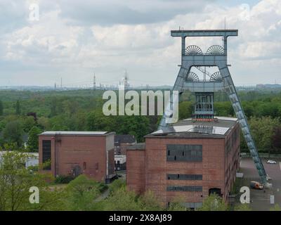 Industriekomplex mit gewundenem Turm und umliegender grüner Landschaft unter bewölktem Himmel, gewundener Turm einer stillgelegten Zeche im grünen Ruhrgebiet, Stockfoto