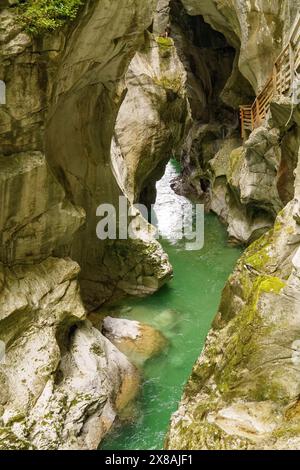 Enge Schlucht mit grünem Fluss, umgeben von massiven Felswänden und einer Brücke an der Seite, wilder Bergbach in einer Schlucht zwischen Felsen und Bäumen, Gos Stockfoto