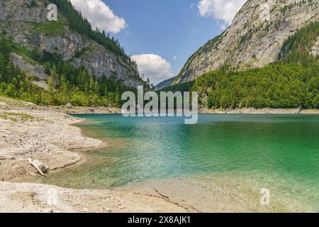 Idyllischer Bergsee mit blauem Wasser, umgeben von steilen, bewaldeten Berghängen und Felswänden, unter bewölktem Himmel, glitzernd grüner Berg lak Stockfoto