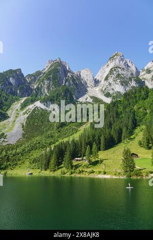 Hohe Berge, grüne Wälder und ein See mit kleinen Hütten am Ufer, klarer Bergsee in den Alpen mit hohen Bergen und grünen Bergen, Gosau, Stockfoto