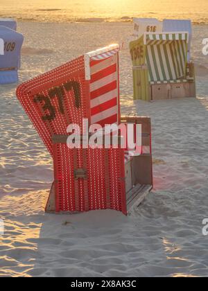 Rot-weiß gestreifte Liege bei Sonnenaufgang an einem Sandstrand mit Meerblick, Sonnenuntergang am Meer mit vielen bunten Liegen am Strand, warm Lig Stockfoto