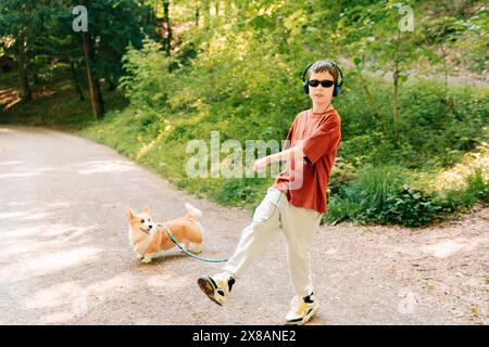 Teenager in Kopfhörern tanzen und spielen mit einem Corgi-Hund im Sommer Stockfoto