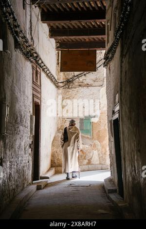 Ein älterer Mann benutzt einen Stock, um eine Gasse in Marrakesch zu entlanggehen. Stockfoto