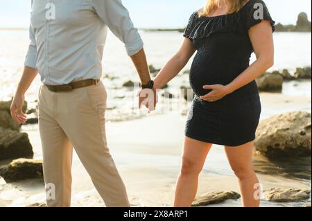 Mitte des verheirateten, schwangeren Paares, die gemeinsam am Strand entlang laufen Stockfoto