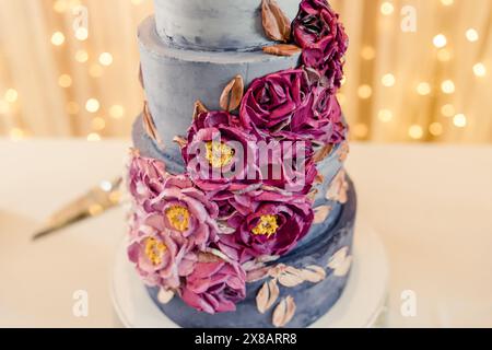 Elegante dreistufige Hochzeitstorte mit violetten Blumendekorationen Stockfoto