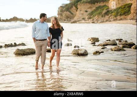 Wunderschönes schwangeres Paar, das am Küstenstrand entlang spaziert Stockfoto