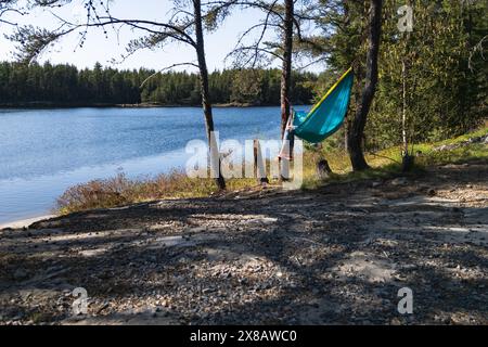 Eine Frau, die sich in einer Hängematte zwischen Bäumen am See entspannt Stockfoto