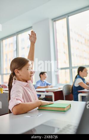 Ein junges Mädchen mit langen Haaren hebt ihre Hand in einem farbenfrohen, lebhaften Klassenzimmer. Stockfoto