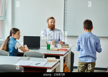 Ein Mann sitzt an einem Schreibtisch vor einer Gruppe von Kindern und engagiert sie in einer lebhaften Klassenzimmer-Umgebung. Stockfoto