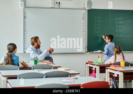 Eine Gruppe von Kindern sitzt aufmerksam an Schreibtischen vor einer Tafel und hört einem männlichen Lehrer zu, der sie in einem hellen und lebhaften cla unterrichtet Stockfoto