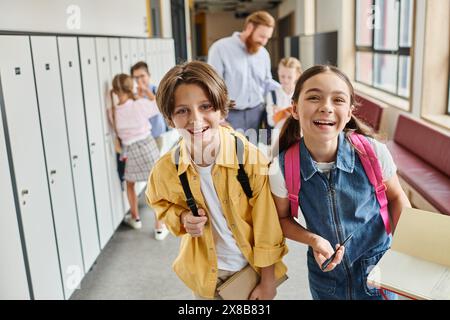 Eine vielfältige Gruppe von Kindern spaziert durch einen Schulflur voller farbenfroher Schließfächer, plaudert und lacht, während sie zur nächsten Klasse aufbrechen. Stockfoto