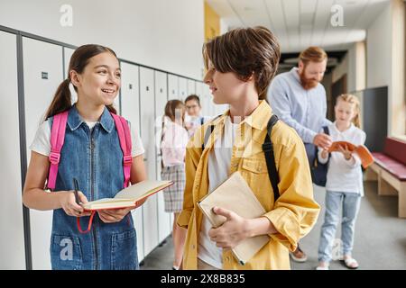 Ein Junge und ein Mädchen, Teil einer Gruppe von Kindern, stehen nebeneinander in einem Flur und warten auf Anweisungen ihres lebhaften Lehrers. Stockfoto