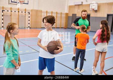 Eine vielfältige Gruppe junger Leute steht um einen Basketballplatz herum, plaudert und lacht, während ein Lehrer sie in einer lebhaften Umgebung unterrichtet. Stockfoto