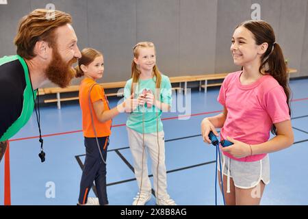 Ein bärtiger Mann unterrichtet eine Gruppe verschiedener Kinder in einem lebhaften Gymnasium und fesselt ihre Aufmerksamkeit mit fesselnden Lektionen. Stockfoto